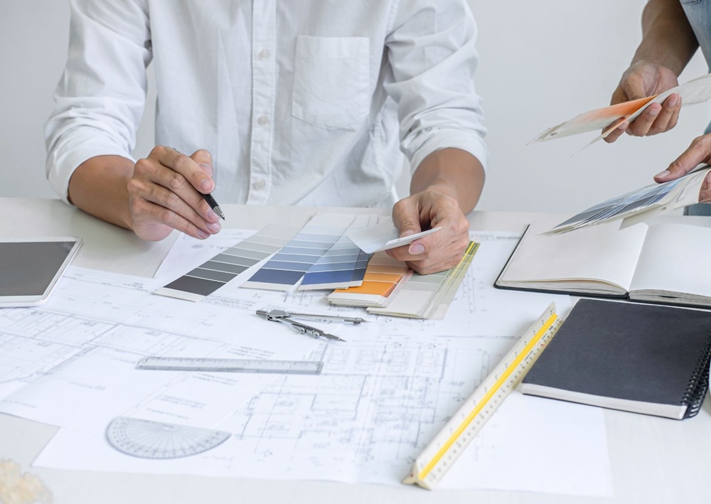 Designers collaborate over architectural plans, color samples, material selections, and measuring tools during project planning.