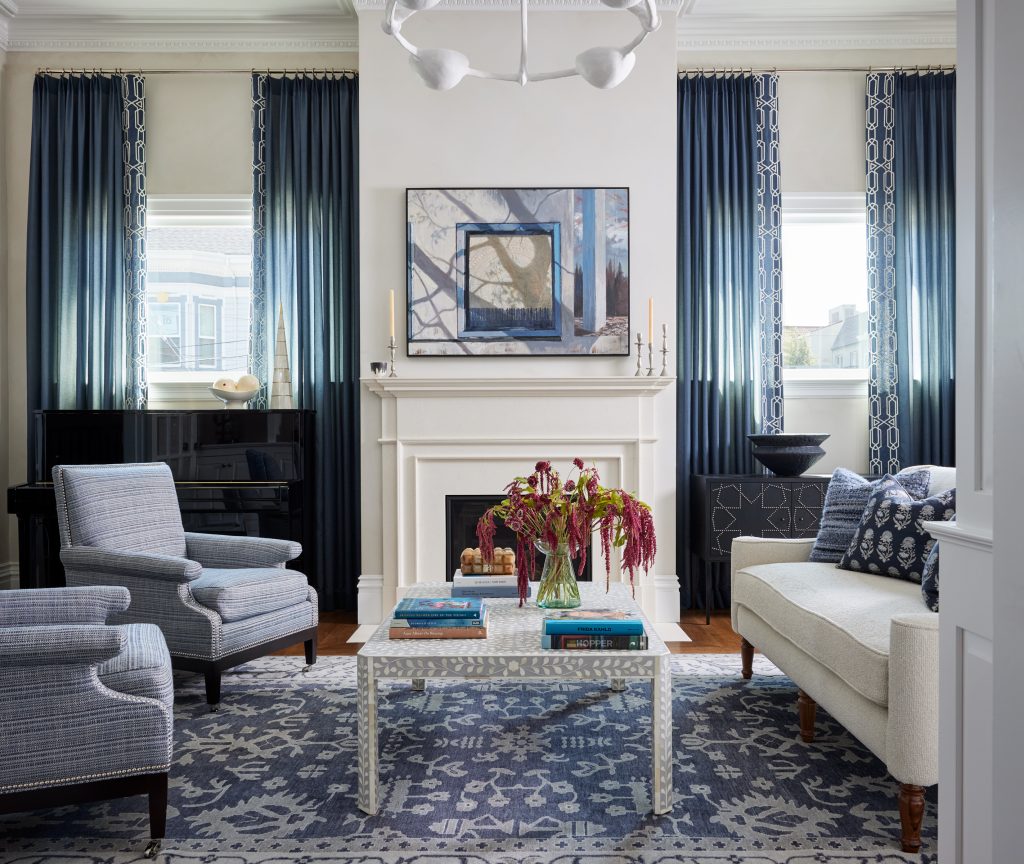 Elegant living room with symmetrical seating, decorative fireplace, patterned rug, and layered furnishings designed by an interior professional.